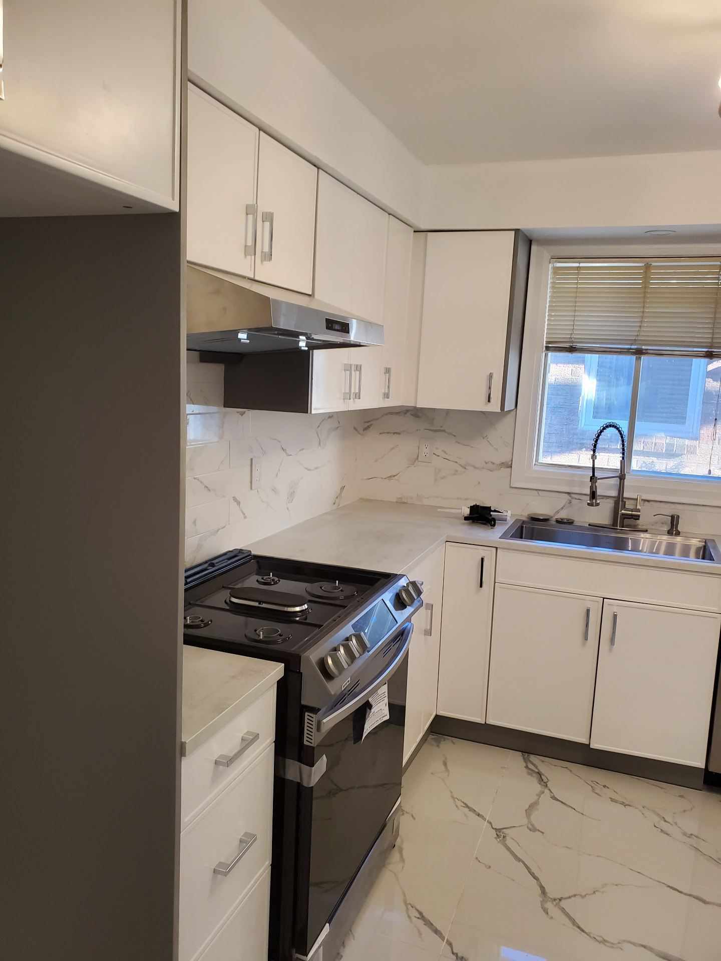 Completed modern kitchen with white cabinets, stainless sink and window