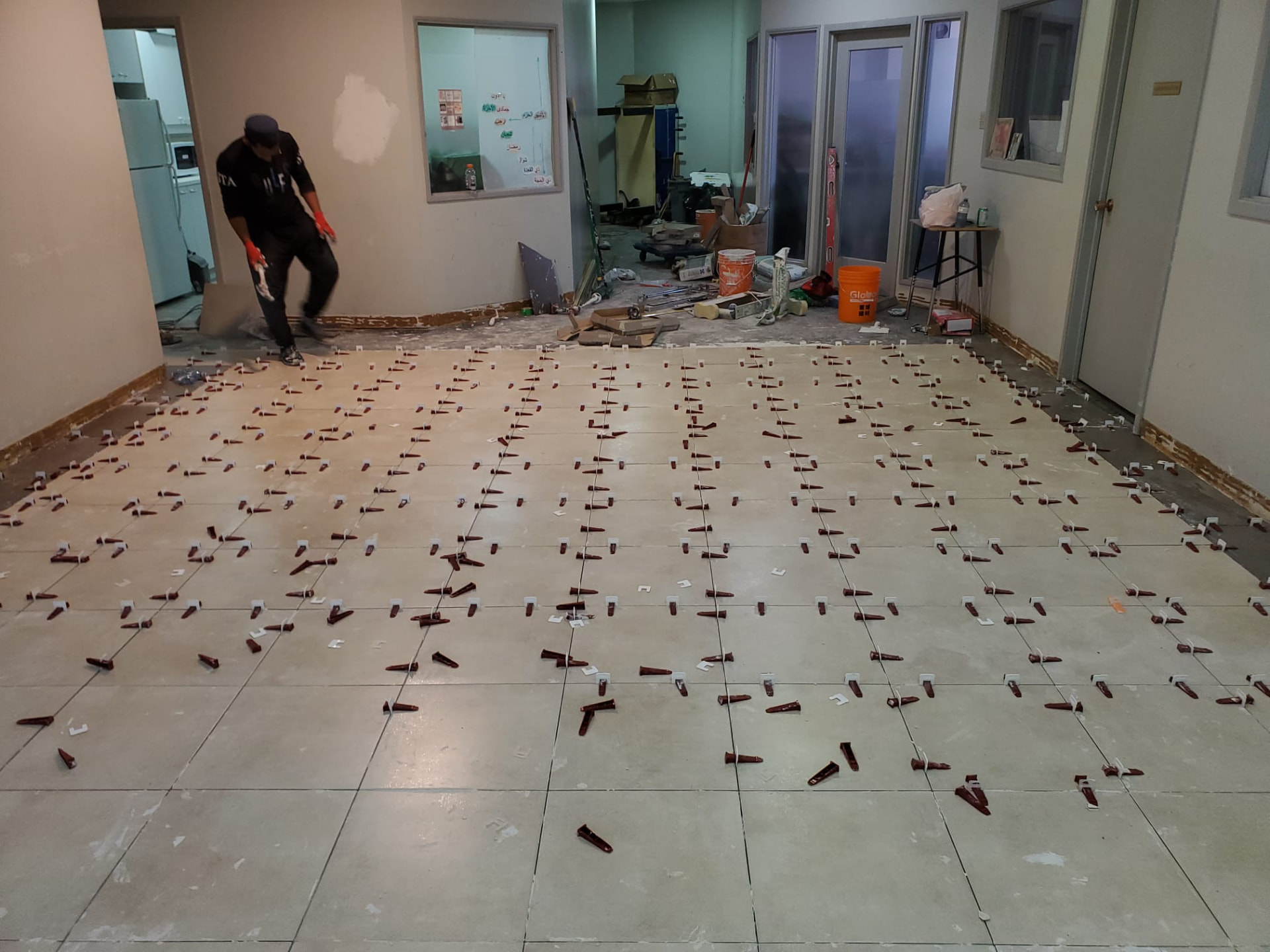 Tile installation progress across a large interior floor with levelling system in place
