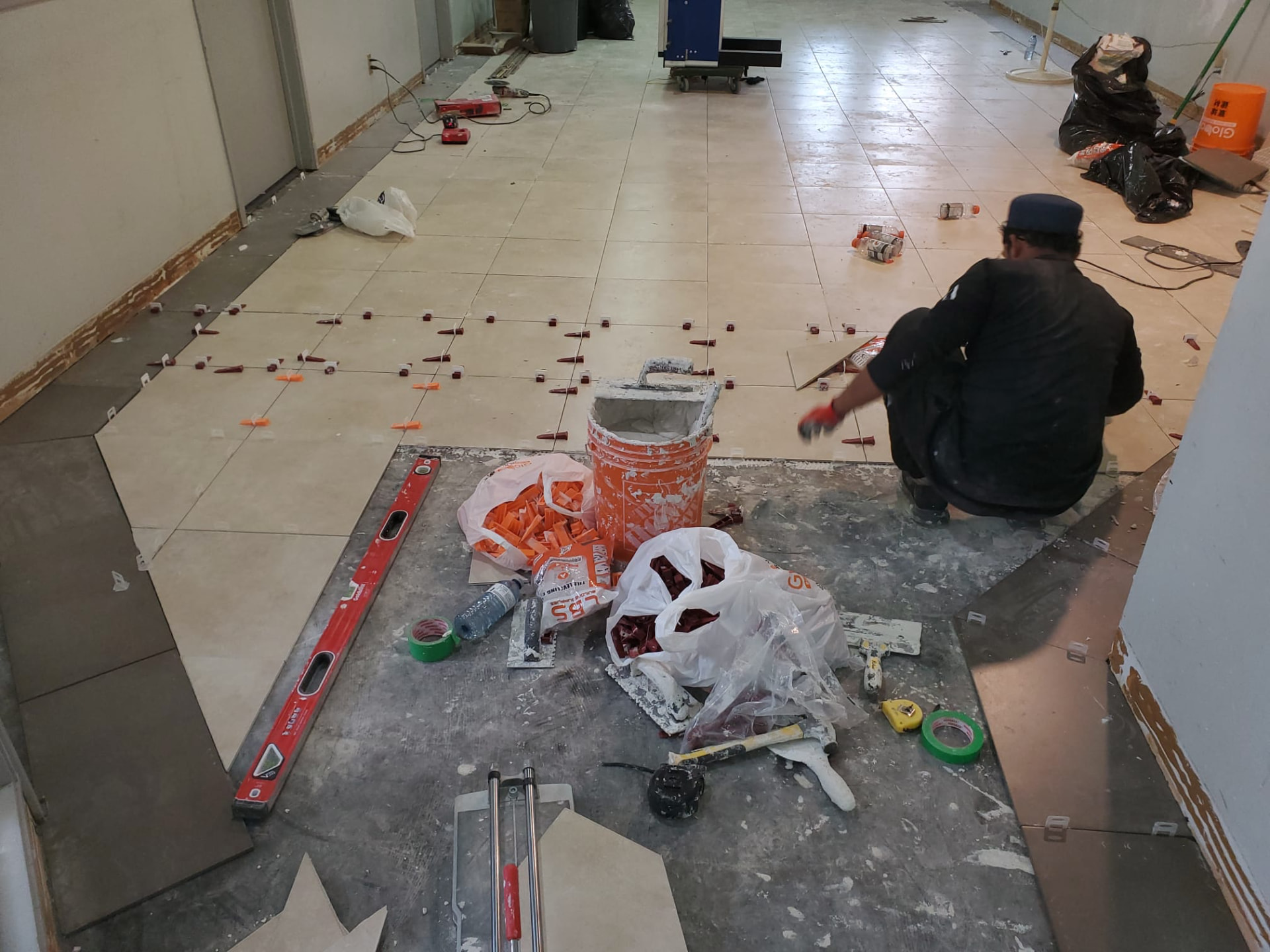 Worker setting large-format floor tile with levelling clips and wedges